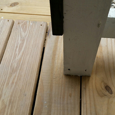 Deck post holding up a roof and it is sitting on the deck boards without a beam  underneath. There should be a direct load path from the roof all the way to the ground and in this case the roof load is resting on 1 inch boards which could fail.